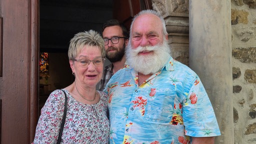 Bärbel und Dieter Koscinski aus Bochum stehen in normaler Alltagskleidung vor einer Kirche.