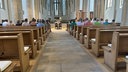 Der große Innenraum einer Kirche ist gefüllt mit Menschen, die einem Paar bei ihrer Trauung zuschauen