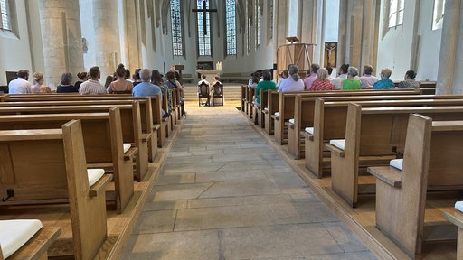 Der große Innenraum einer Kirche ist gefüllt mit Menschen, die einem Paar bei ihrer Trauung zuschauen