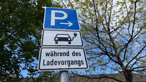 Ein blaues Parkplatz-Schild, darunte ein Schild mit einem Elektroauto und der Aufschrift "während des Ladevorgangs"