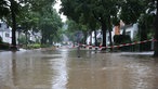 Eine überflutete Straße in Erkrath ist in der Mitte mit einem rot-weißen Flatterband abgesperrt.