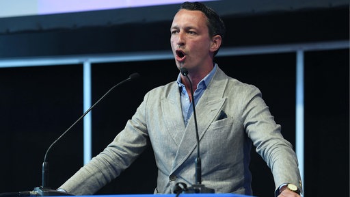 AfD-Politiker Matthias Helferich steht vor einem Podium und spricht in zwei Mikrofone.