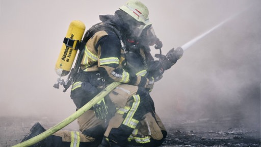 Zwei Feuerwehrleute mit Wasserschlauch, eingehüllt in Brandrauch