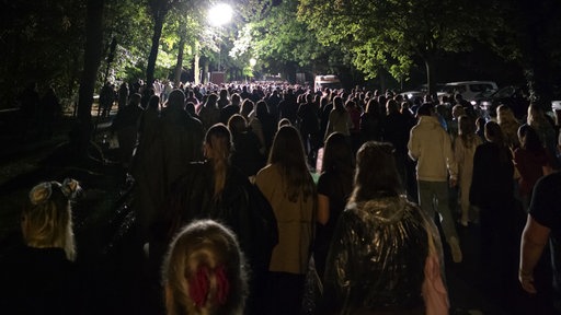 Eine Gruppe Menschen läuft auf einer Straße durch einen Wald, im Hintergrund leutet eine Straßenlaterne