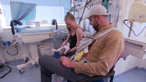 Eine Frau und ein Mann sitzen im Uniklinikum mit ihren beiden Babys auf dem Arm