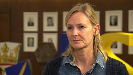 eine Frau mit blonden Haaren, im Hintergrund hängen mehrere Bilder an der Wand