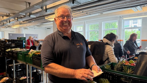 Jörg Sartor steht lächelnd vor Lebensmittelkisten bei der Essener Tafel.