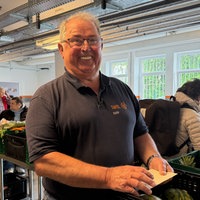 Jörg Sartor steht lächelnd vor Lebensmittelkisten bei der Essener Tafel.