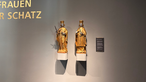 Zwei goldene Figuren auf Sockeln an einer Museumswand