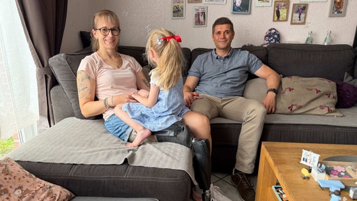 Janine Rähl sitzt mit ihrer Tochter und ihrem Mann auf einem Sofa