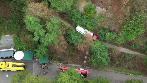 Luftaufnahme eines Tanklasters, der auf einem schmalen Waldweg in Essen gefährlich nahe an einem Abhang feststeckt, während Einsatzkräfte das Fahrzeug sichern.