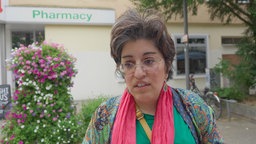 Eine Frau mit rosa Halstuch steht vor einer Apotheke