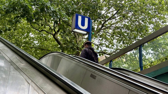 Schild einer U-Bahn-Station in der Essener Innenstadt mit Rolltreppe davor, auf der ein Fahrgast steht