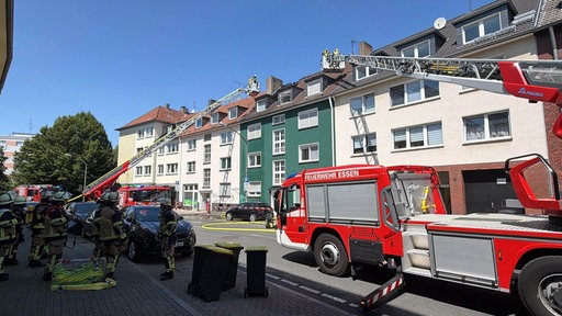Zwei Leiterwagen der Feuerwehr stehen vor einem Haus im Essener Südviertel und löschen das Feuer in einem Dachstuhl