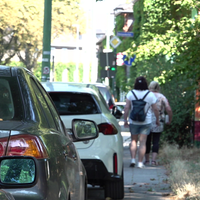 Eine Reihe Autos parkt an einem Gehweg, der dadurch sehr beschränkt ist.