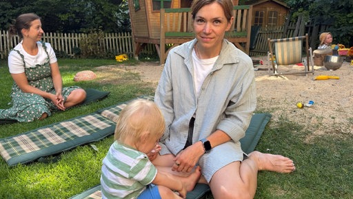 Eine Mutter sitzt mit ihrem Kind im Garten