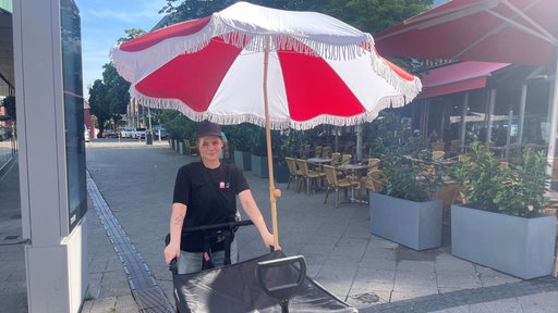 Streetworkerin Emeli Kaebler schiebt einen Bollerwagen gefüllt mit Sonnencreme und Wasser