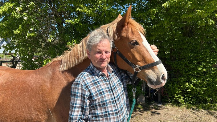 Volker Neuhaus steht neben einem braunen Pferd, er hat einen Arm um dessen Kopf gelegt