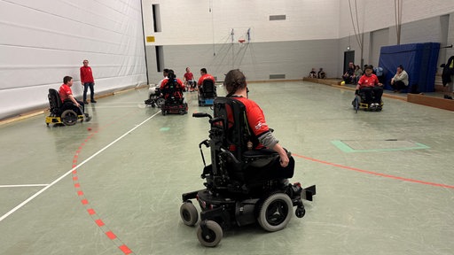 Mehrere Spieler spielen in ihren elektrischen Rollstühlen auf dem Feld. 