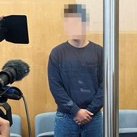 Das Bild zeigt den Angeklagten im Gerichtssaal, wo er von einem Fernsehteam gefilmt wird.