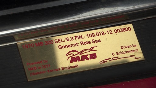 Goldene Plakette im Türeinstieg eines Autos, in der Mitte die Aufschrift "Genannt: Rote Sau", unten rechts eine Unterschrift von Clemens Schickentanz.