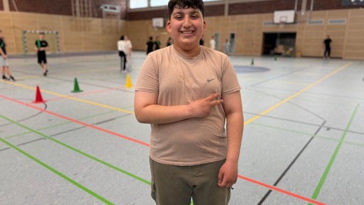 Schüler Aras Mohamad steht in der Sporthalle und freut sich über die neuen Handball-Wurftechniken 