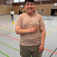 Schüler Aras Mohamad steht in der Sporthalle und freut sich über die neuen Handball-Wurftechniken 