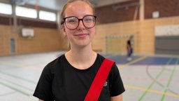 Schülerin Emily steht lächelnd in der Sporthalle