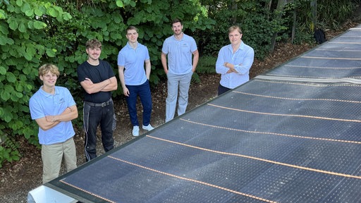Die fünf Gründer von "Solarmarkisen" stehen im Halbkreis um eine dunkle, ausgerollte Markise