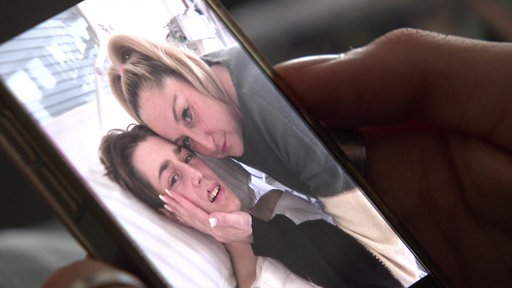 Kopf eines jungen Mannes im Krankenbett neben dem Kopf einer Frau 