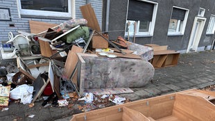 Auf dem Bürgersteig vor einem Haus liegt ein großer Müllberg mit alten Möbeln, Holzbrettern, Tüten und Geschirr