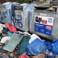 Vor Papiercontainern liegt eine große Menge Müll, z.B. Papier, blaue Säcke und Folien