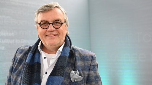 Der Komiker und Autor Hape Kerkeling steht am 29.03.2025 auf der Literaturbühne in der Glashalle der Buchmesse Leipzig und lächelt.