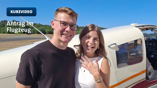 Ein junges Paar steht vor einem Flugzeug