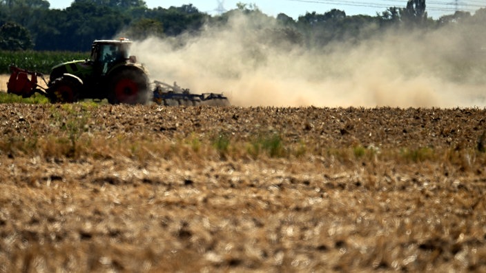 Ein Traktor zieht bei der Arbeit auf dem Feld eine dicke Staubwolke hinter sich her