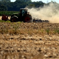 Ein Traktor zieht bei der Arbeit auf dem Feld eine dicke Staubwolke hinter sich her