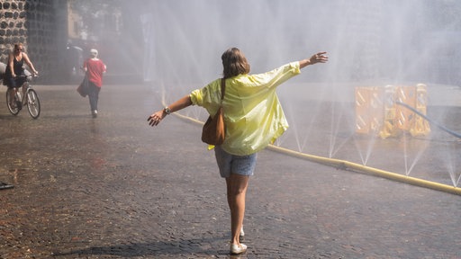 Eine Frau mit gelber Bluse erfrischt sich bei sommerlicher Hitze in Köln.