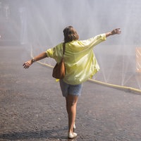Eine Frau mit gelber Bluse erfrischt sich bei sommerlicher Hitze in Köln.