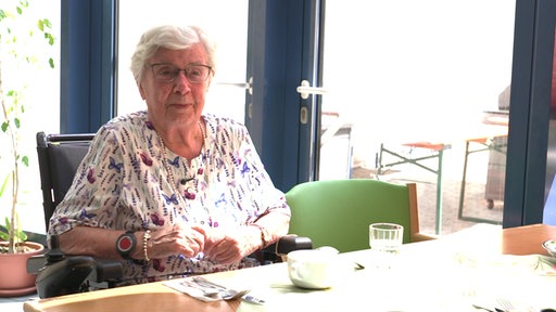 Alte Dame sitzt an einem Esstisch mit Tasse in der Hand