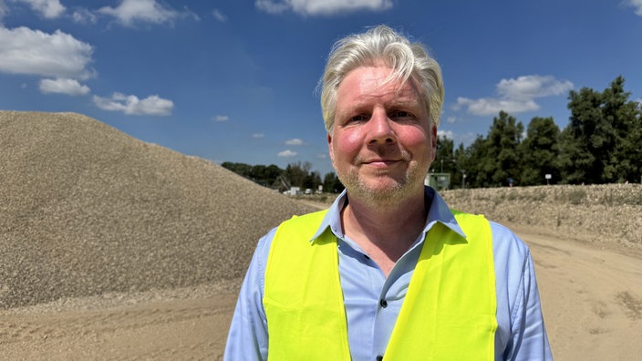 Sascha Kruchen, Zukunft Niederrhein, Initiative der Sand- und Kiesunternehmen, steht vor Kieshügeln und trägt eine gelbe Warnweste.