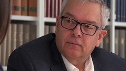 Dirk Schwane ist Anwalt. Er trägt eine Brille und einen schwarzen Anzug.