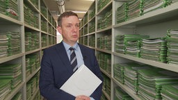 Andreas Ostheimer, Präsident am Sozialgericht in Duisburg, steht zwischen Schränken mit grünen Akten.