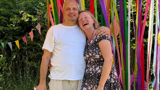 Ein Mann und eine Frau, ein Hochzeitspärchen in Rösrath, umarmen sich - dahinter sind bunte Girlanden