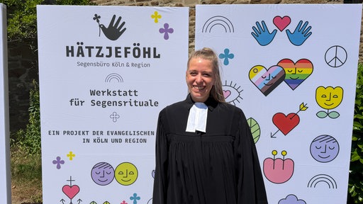 Eine evangelische Pfarrerin steht vor einer bunten Wand mit Logos