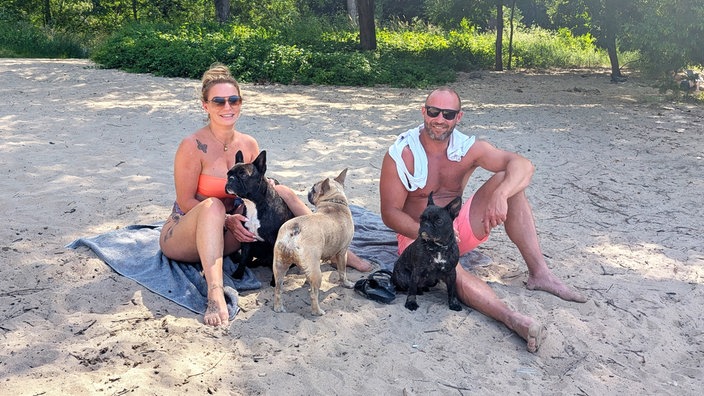 Lisa Schenk und Thomas Blohm sitzen am Strand der Rodenkirchener Riviera.