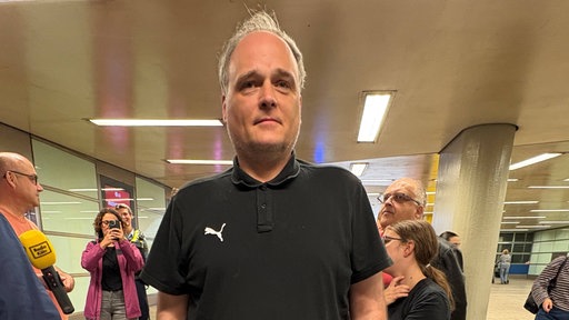 Mann steht vor einer Gruppe Menschen im Kölner Hauptbahnhof und schaut in die Kamera