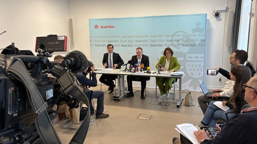 mehrere Menschen sitzen an einem Tisch und halten eine Pressekonferenz