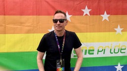Uwe Weiler, der CSD-Geschäftsführer steht vor einer Cologne Pride Flagge.