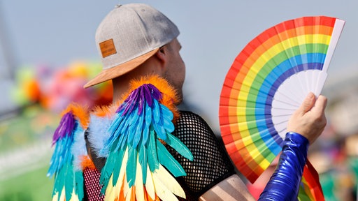 Ein CSD-Teilnehmer hält in  Köln einen Regenbogen-Fächer in der Hand.