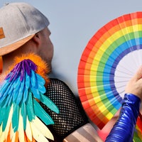 Ein CSD-Teilnehmer hält in  Köln einen Regenbogen-Fächer in der Hand.